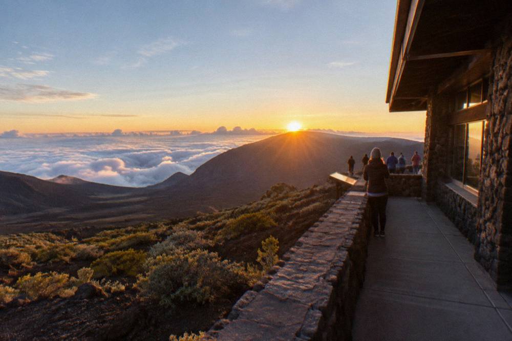 Sun breaking over Haleakala crater with clouds below the summit